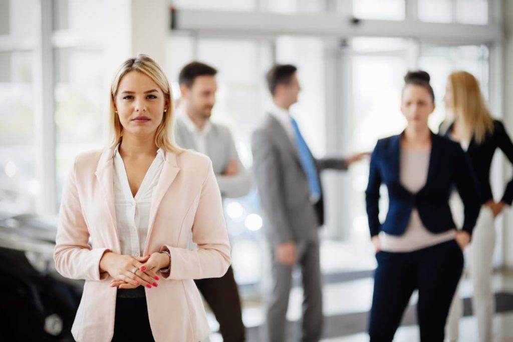 Femme d’affaires confiante en avant-plan avec une équipe de professionnels en arrière-plan dans un environnement d’entreprise.